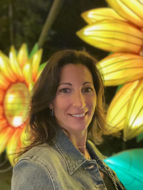 Dawn, wearing a jean jacket, in front of a yellow sunflower background